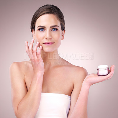 Buy stock photo Studio portrait of an attractive young woman applying moisturizer to her face against a pink background