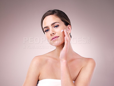 Buy stock photo Studio shot of an attractive young woman applying moisturizer to her face against a pink background