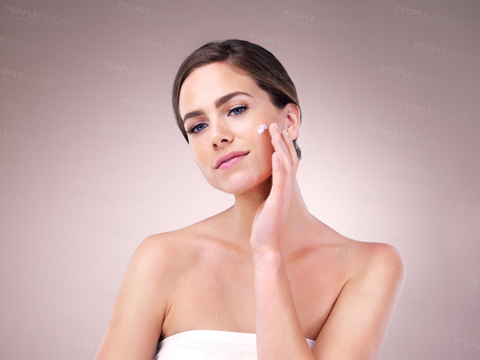 Buy stock photo Studio shot of an attractive young woman applying moisturizer to her face against a pink background