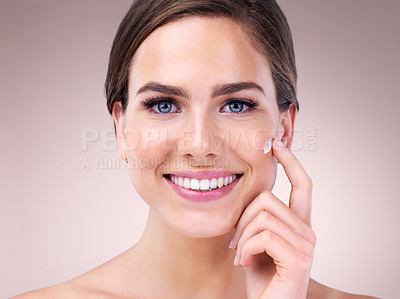 Buy stock photo Studio portrait of an attractive young woman applying moisturizer to her face against a pink background