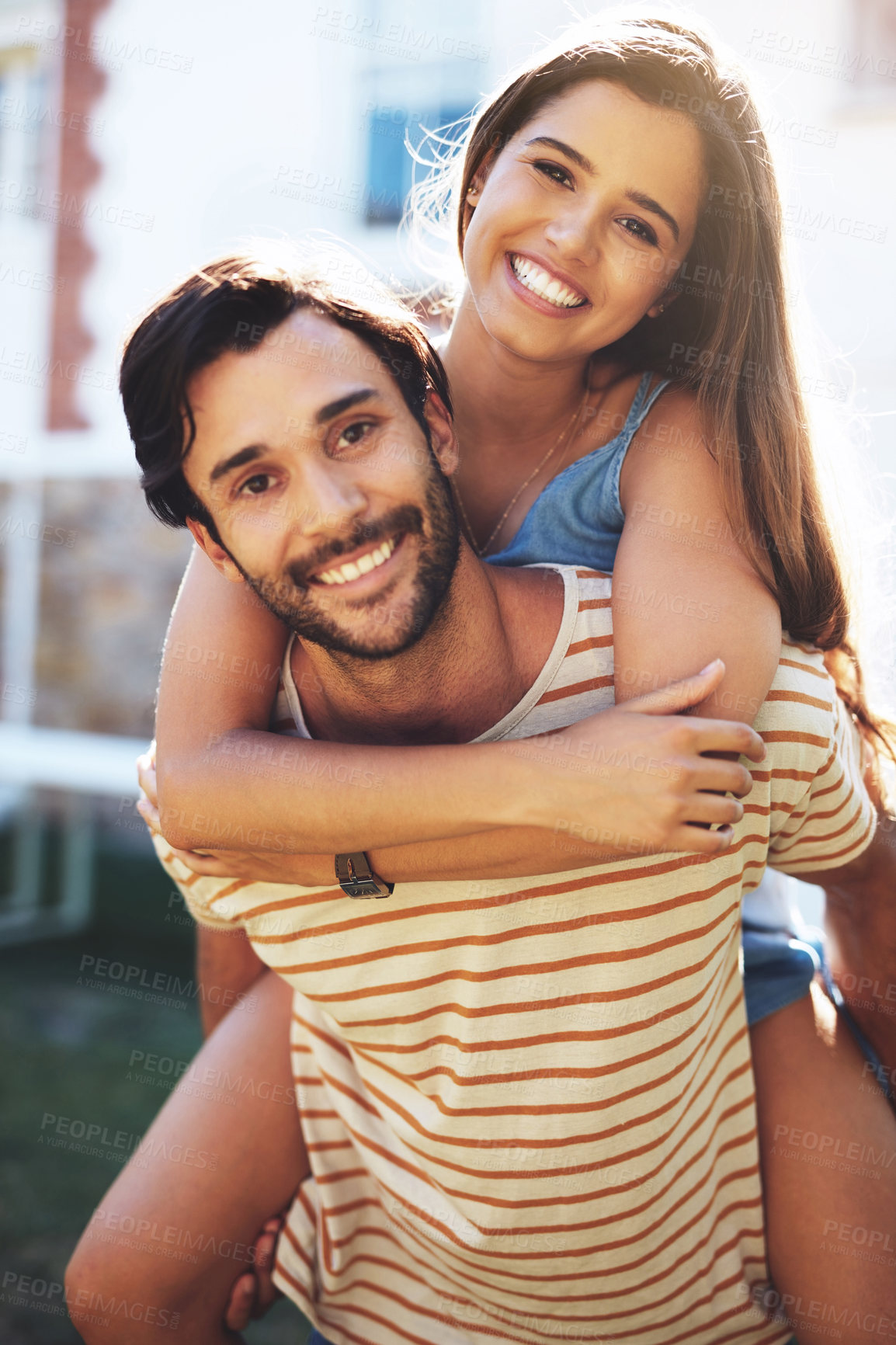 Buy stock photo Portrait of a happy young man giving his girlfriend a piggyback ride outside