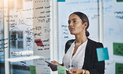 Buy stock photo Shot of a young businesswoman using a digital tablet while brainstorming notes on a glass wall in an office