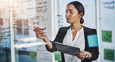 Buy stock photo Shot of a young businesswoman using a digital tablet while brainstorming notes on a glass wall in an office