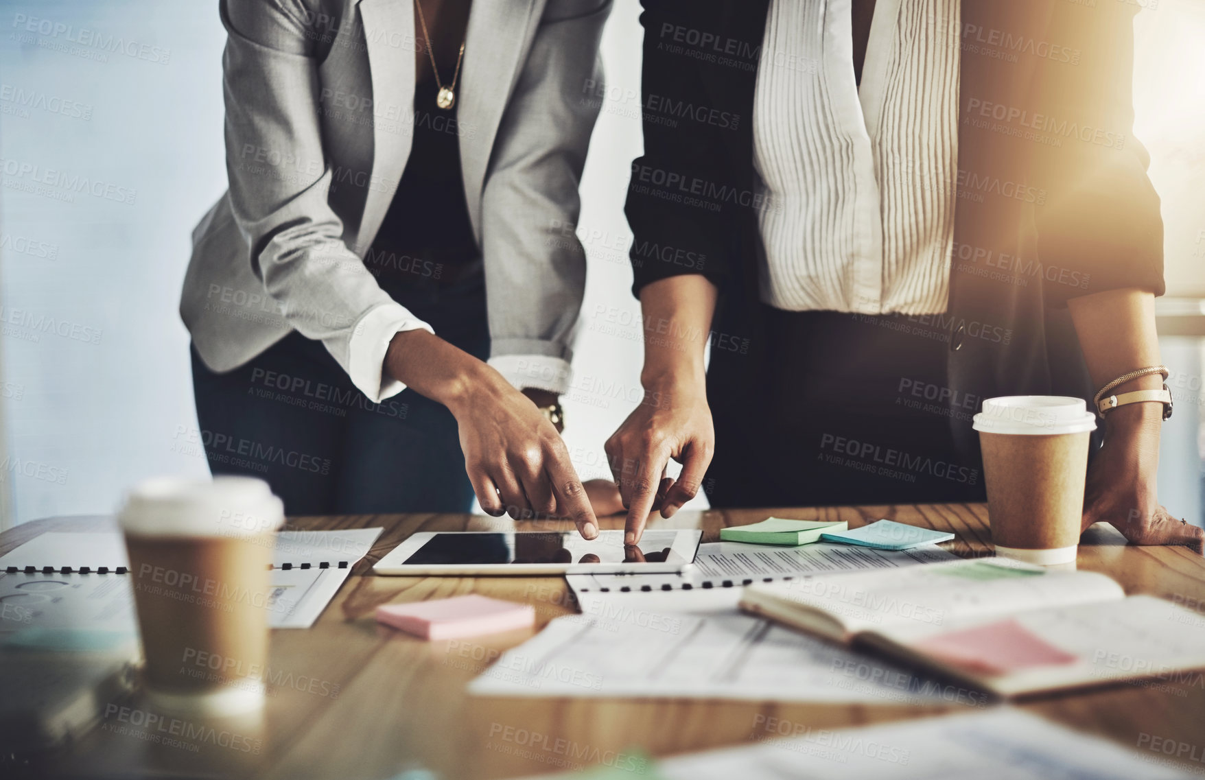 Buy stock photo Closeup shot of two businesswomen using a digital tablet while going through paperwork in an office