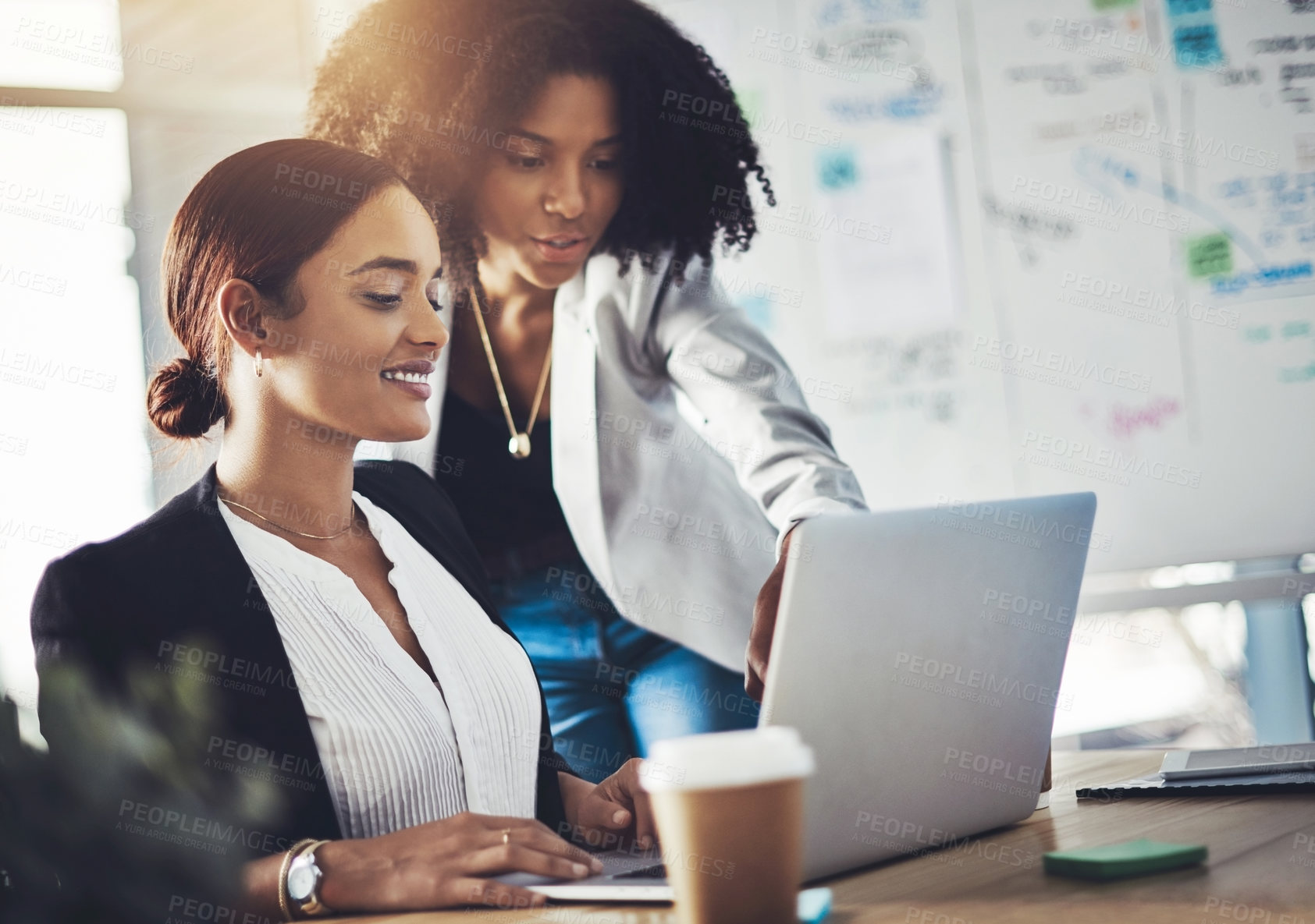 Buy stock photo Shot of two businesswomen working together on a laptop in an office