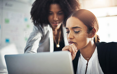 Buy stock photo Shot of two businesswomen working together on a laptop in an office