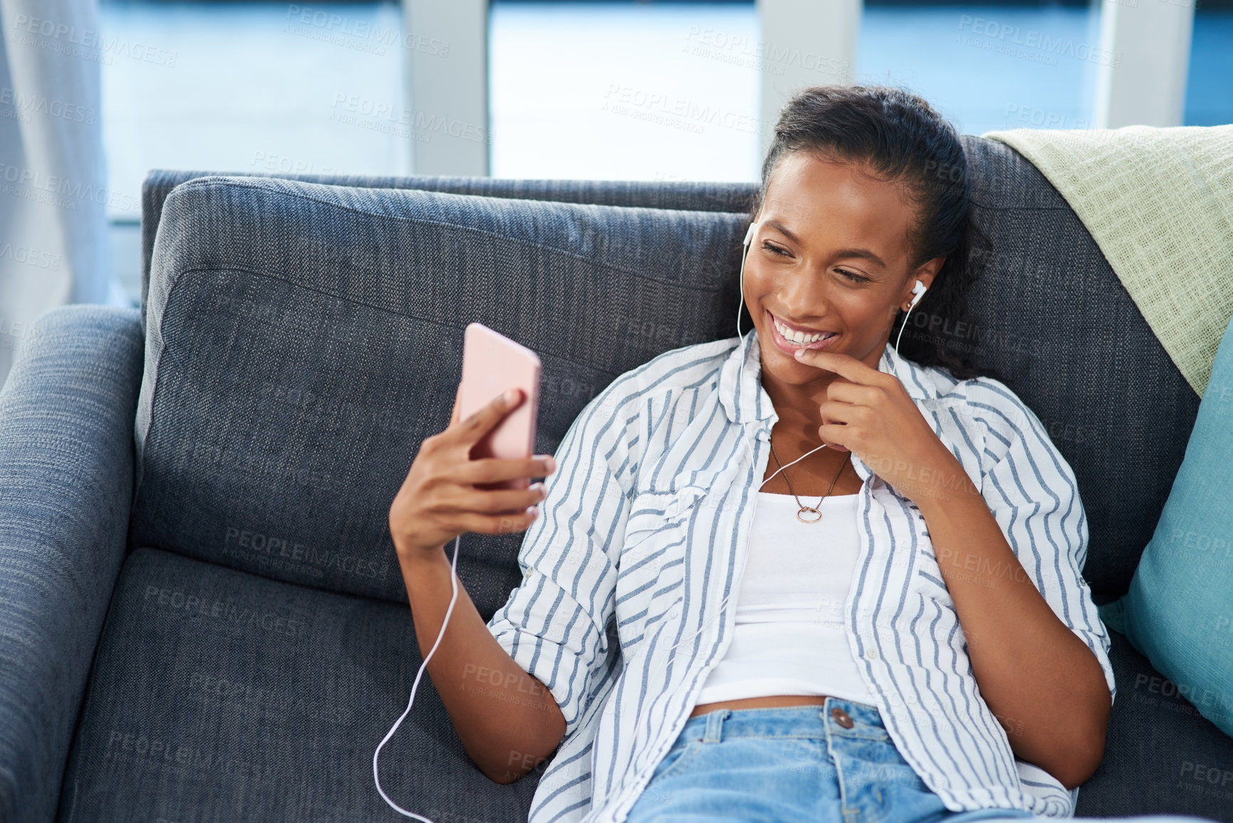 Buy stock photo Shot of a young woman wearing earphones while using a cellphone at home