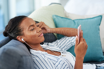 Buy stock photo Shot of a young woman wearing earphones while using a cellphone at home
