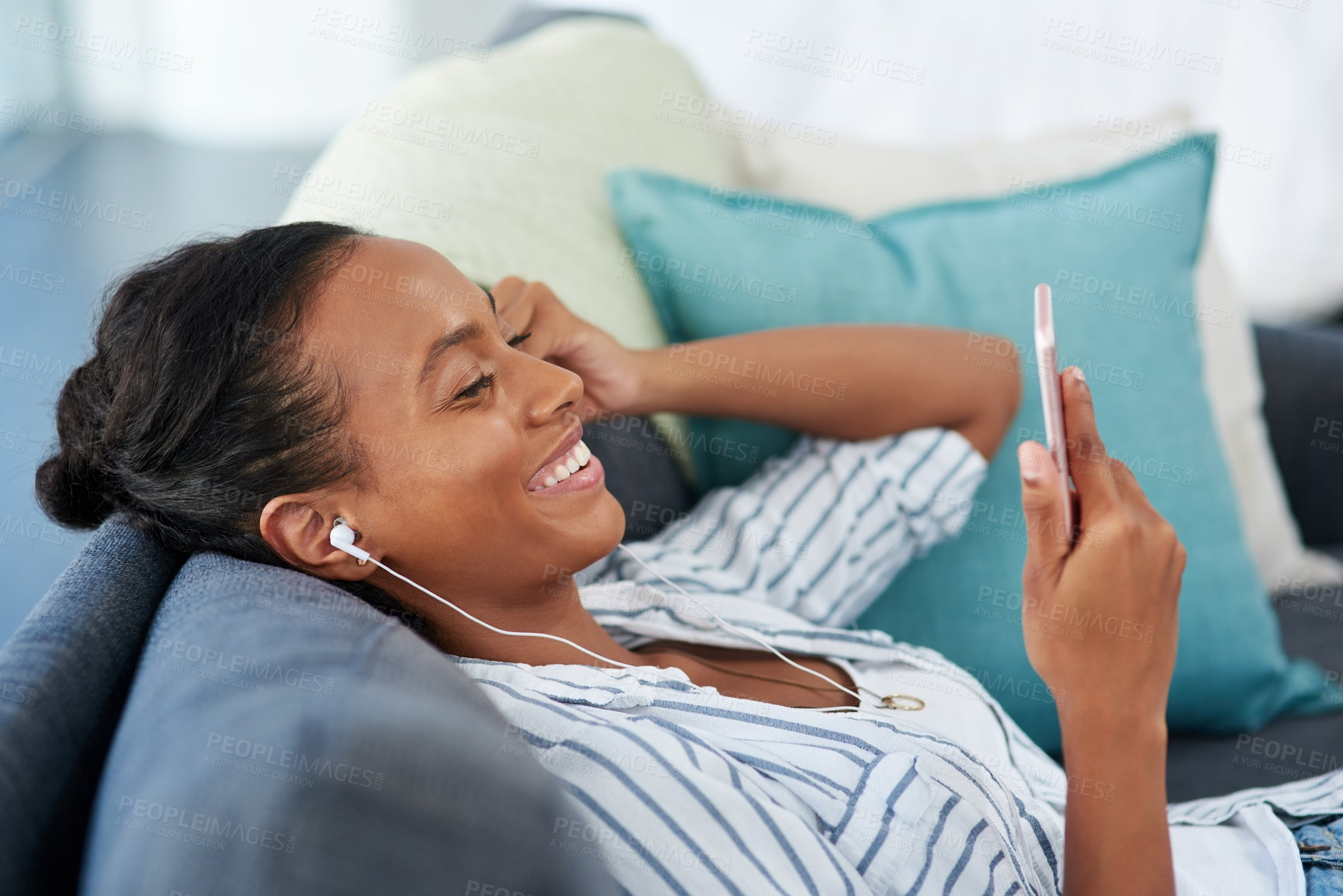 Buy stock photo Woman, smartphone and smiling on couch with earphones, radio and mobile app for audio on weekend break in house. Screen, watching and content video on social media, music streaming and lounge