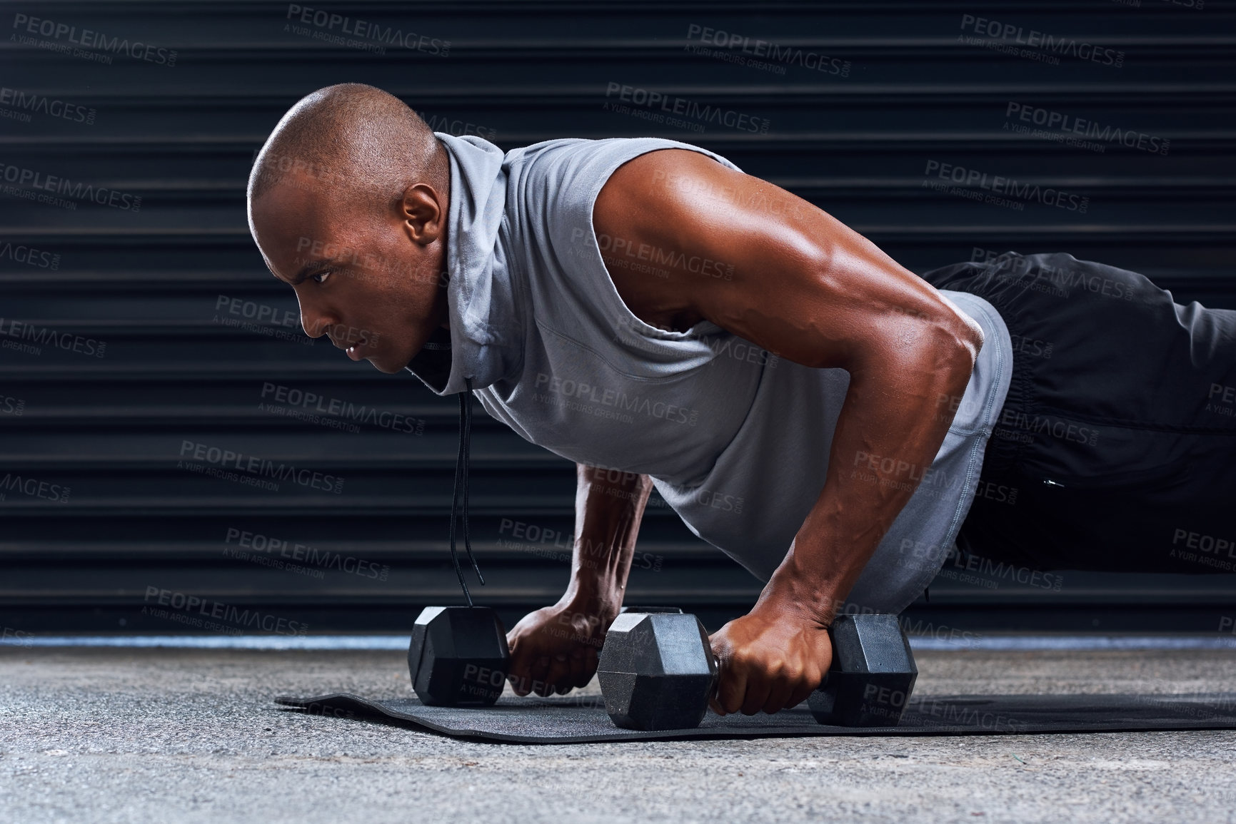 Buy stock photo Shot of a sporty young man working out with dumbbells as part of his exercise routine