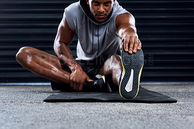 Buy stock photo Shot of a sporty young man stretching his legs as part of his exercise routine