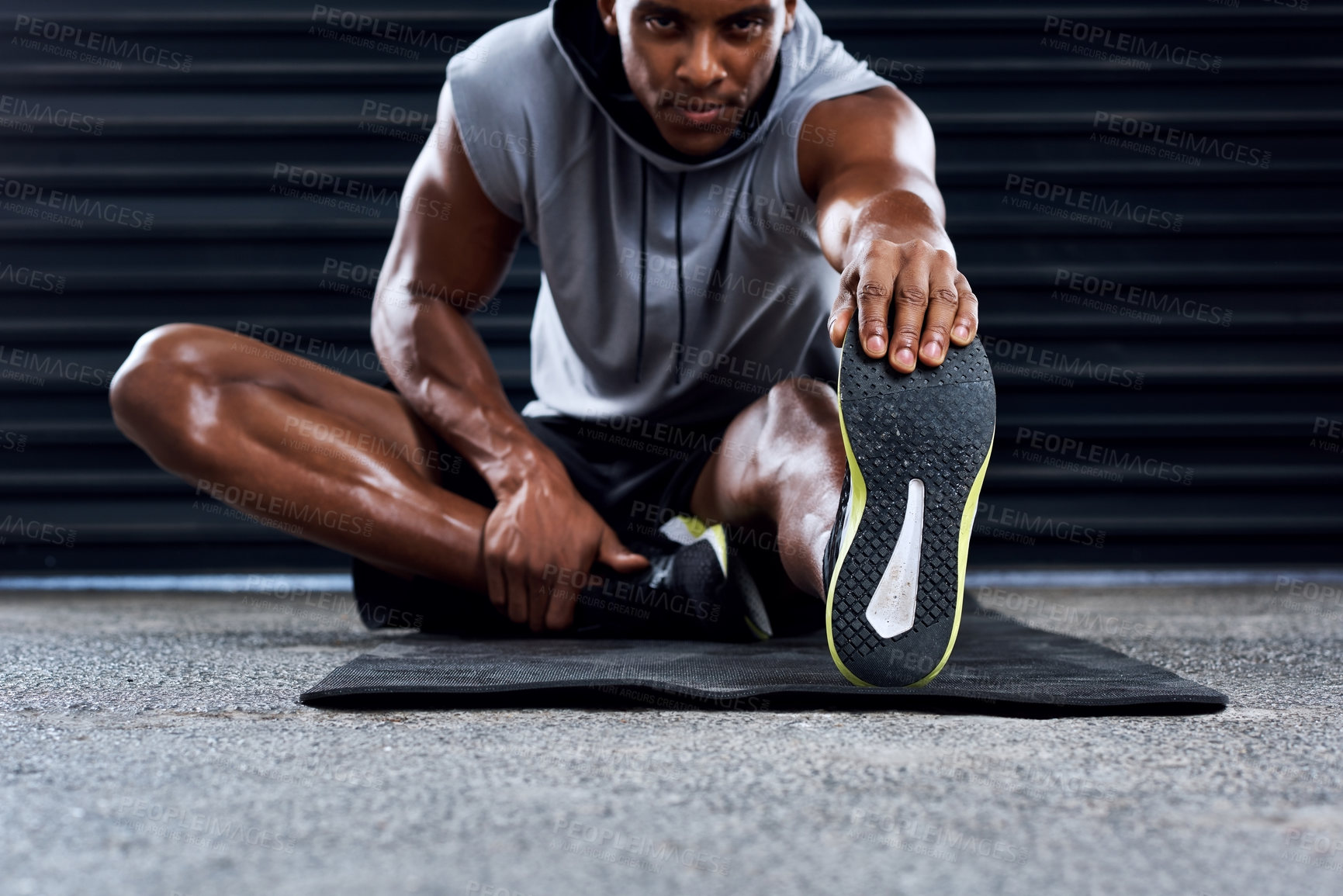 Buy stock photo Shot of a sporty young man stretching his legs as part of his exercise routine