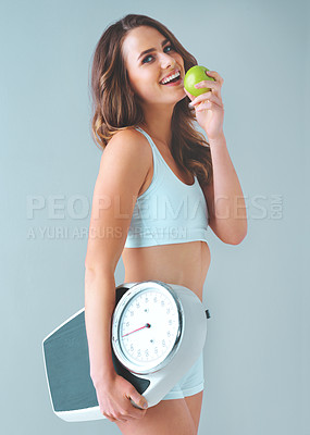 Buy stock photo Studio shot of a healthy young woman holding a scale and an apple against a grey background