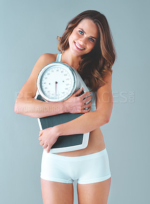 Buy stock photo Studio shot of a healthy young woman smiling and holding a scale against a grey background