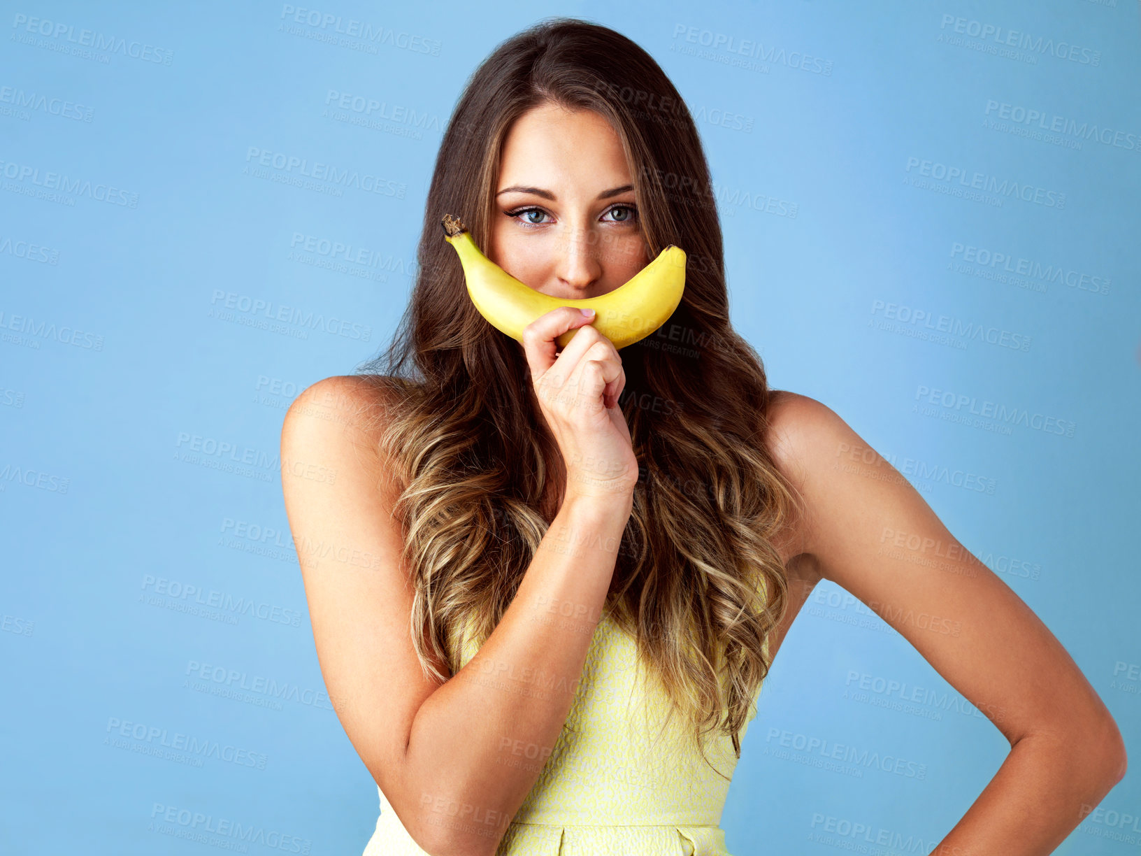 Buy stock photo Studio shot of an attractive young woman with a banana for a smile against a blue background