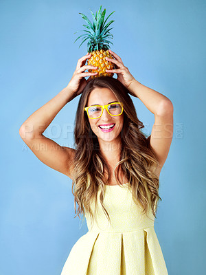 Buy stock photo Studio shot of a young woman balancing a pineapple on her head against a blue background
