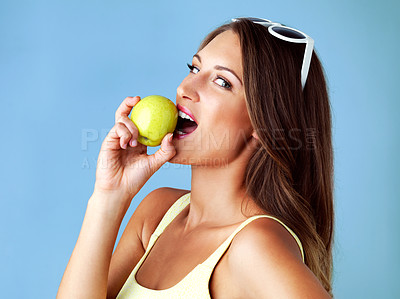 Buy stock photo Studio shot of an attractive young woman biting an apple against a blue background