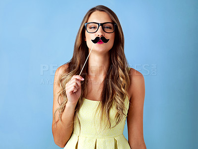 Buy stock photo Studio shot of a young woman holding a moustache prop to her face against a blue background