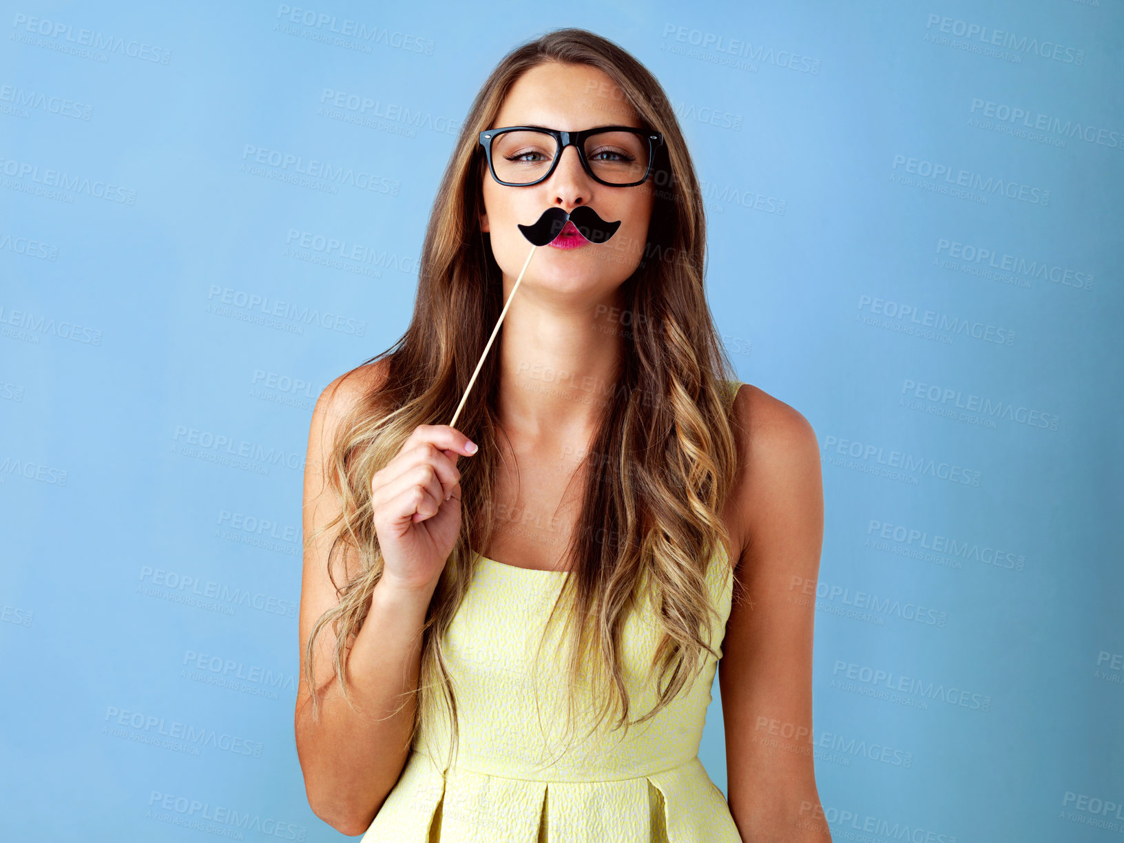 Buy stock photo Studio shot of a young woman holding a moustache prop to her face against a blue background