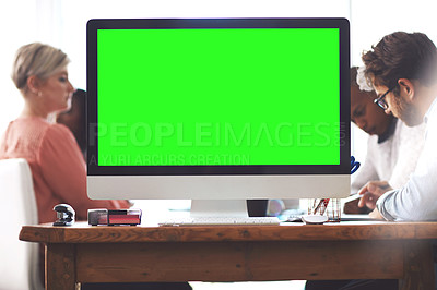 Buy stock photo Shot of a computer with a green screen on a table in an office with businesspeople in the background