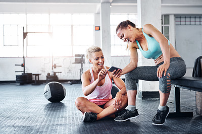 Buy stock photo Shot of two women looking at something on a cellphone in a gym