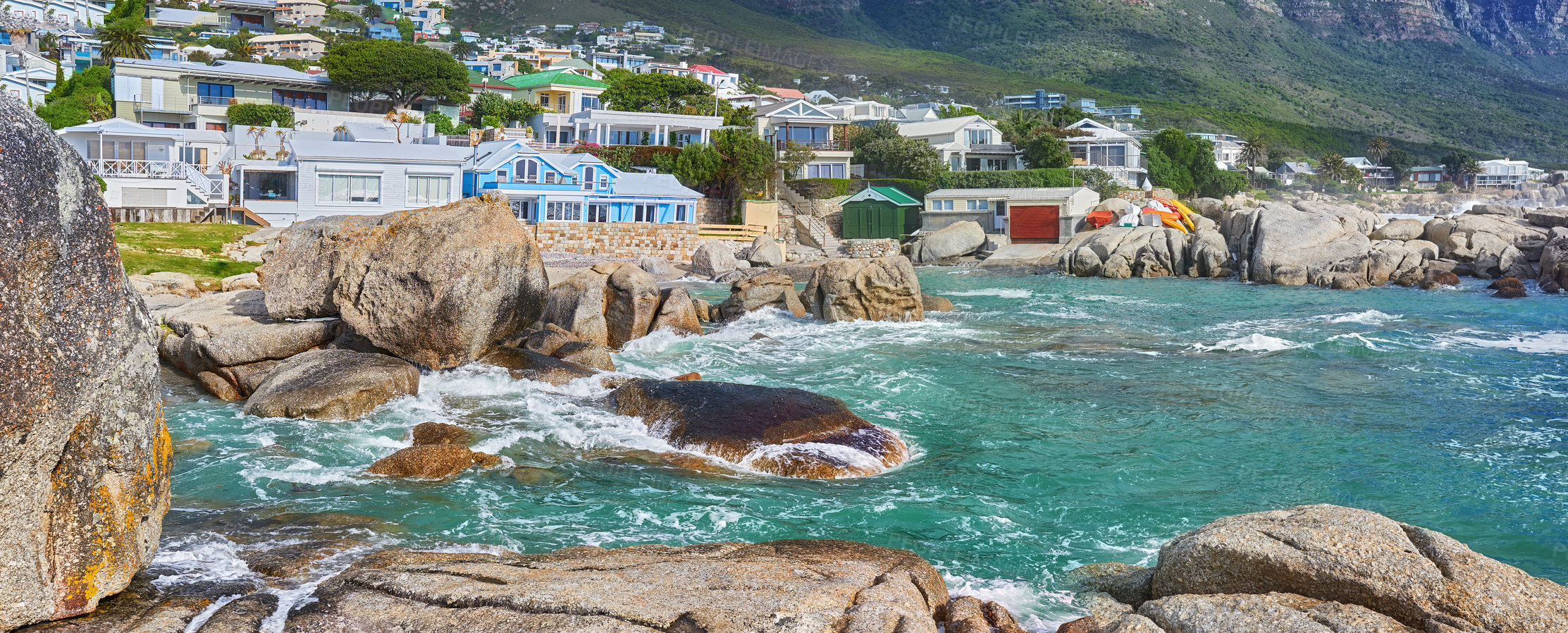 Buy stock photo Scenic view of sea, rocks and residential buildings in Camps Bay Beach, Cape Town, South Africa. Tidal ocean waves washing over shoreline rocks and boulders. Overseas travel and tourism destination