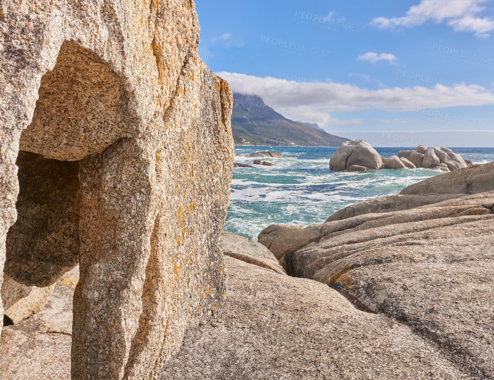 Buy stock photo A rocky shore and a seascape view of the ocean with blue sky copy space and a mountain in the background in Camps Bay, Cape Town, South Africa. Calm, serene, tranquil beach and nature scenery