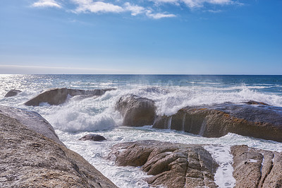 Buy stock photo A rocky shore and a view of the ocean with waves, blue sky copy space, and a horizon in the background in Camps Bay, Cape Town, South Africa. Calm, serene, tranquil beach and nature scenery