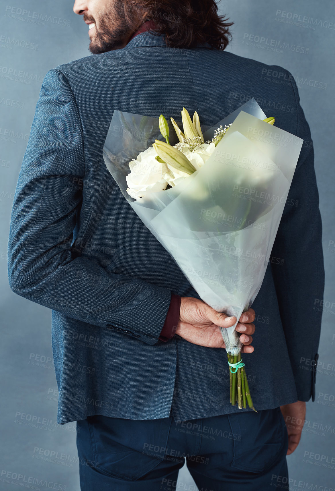 Buy stock photo Studio shot of a stylishly dressed young man holding a bouquet of flowers behind his back against a gray background