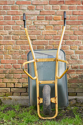 Buy stock photo Garden wheelbarrow leaning against a red brick wall in a home backyard. Landscaping equipment and tools to carry and transport soil, manure, compost and fertilizer. Used to lift construction supplies