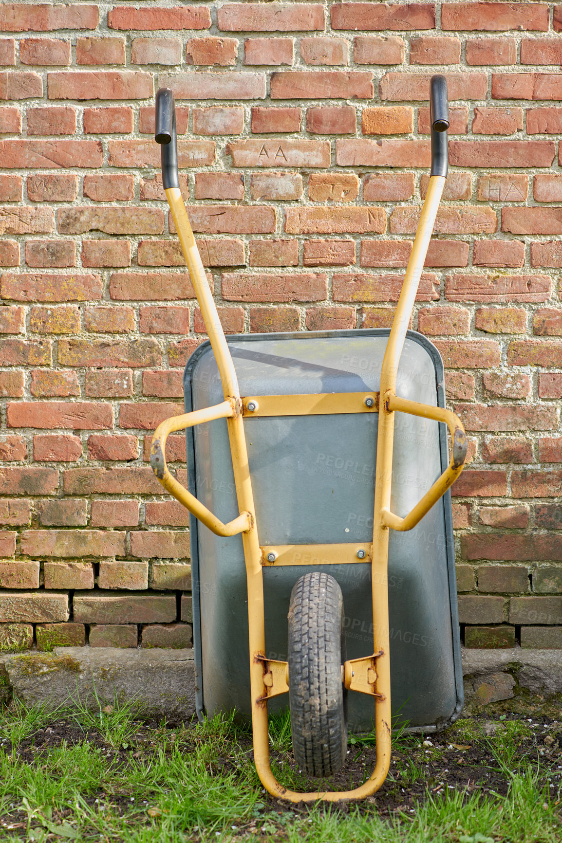 Buy stock photo Garden wheelbarrow leaning against a red brick wall in a home backyard. Landscaping equipment and tools to carry and transport soil, manure, compost and fertilizer. Used to lift construction supplies