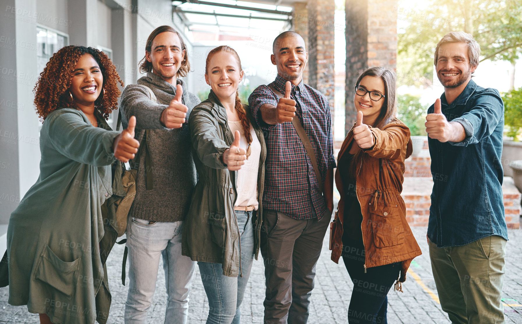 Buy stock photo Portrait of a group of happy young students giving thumbs up together on campus