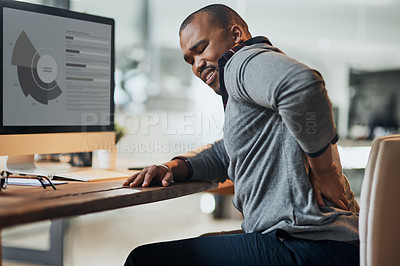 Buy stock photo Shot of a young businessman suffering from a backache while working at his desk in his office