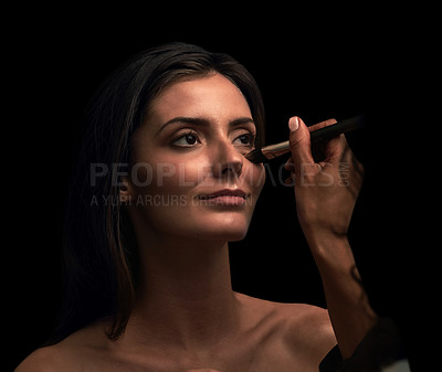 Buy stock photo Studio shot of an attractive young woman having makeup applied on her face against a dark background