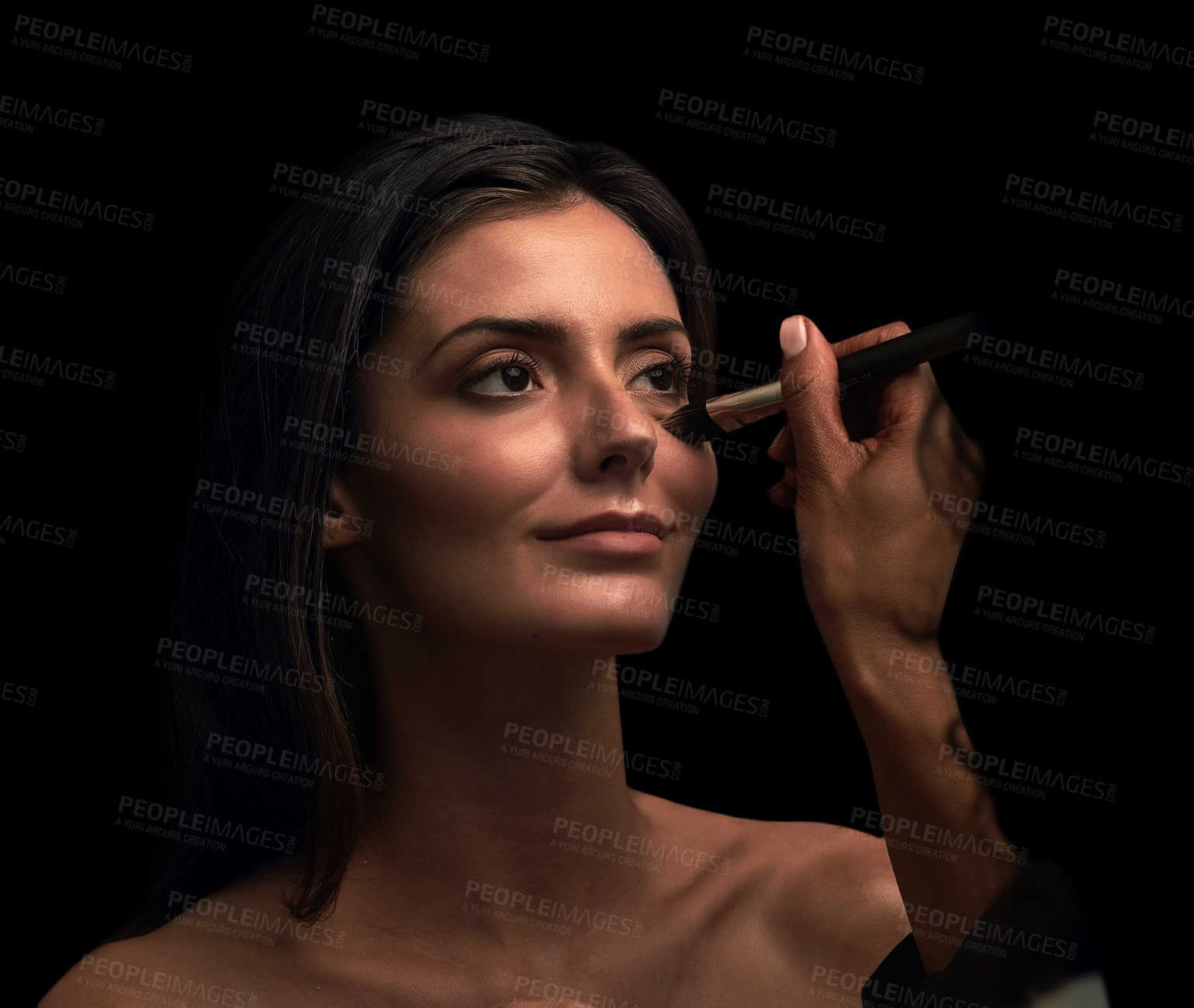Buy stock photo Studio shot of an attractive young woman having makeup applied on her face against a dark background