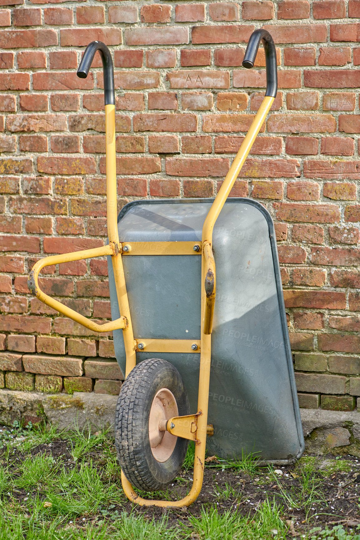 Buy stock photo Garden wheelbarrow leaning against a red brick wall in a home backyard. Landscaping equipment and tools to carry and transport soil, manure, compost and fertilizer. Done cleaning a landscaped yard