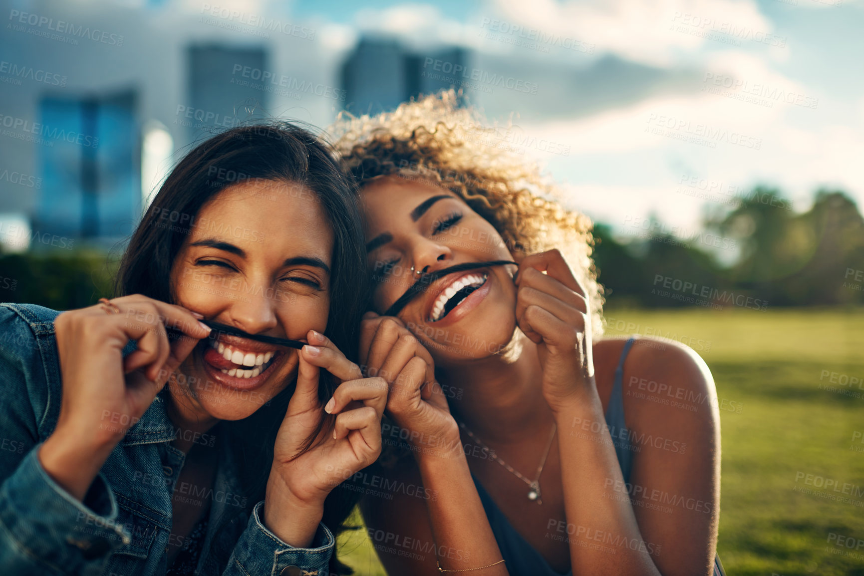 Buy stock photo Cropped portrait of two attractive young girlfriends making a moustache with their hair in a park