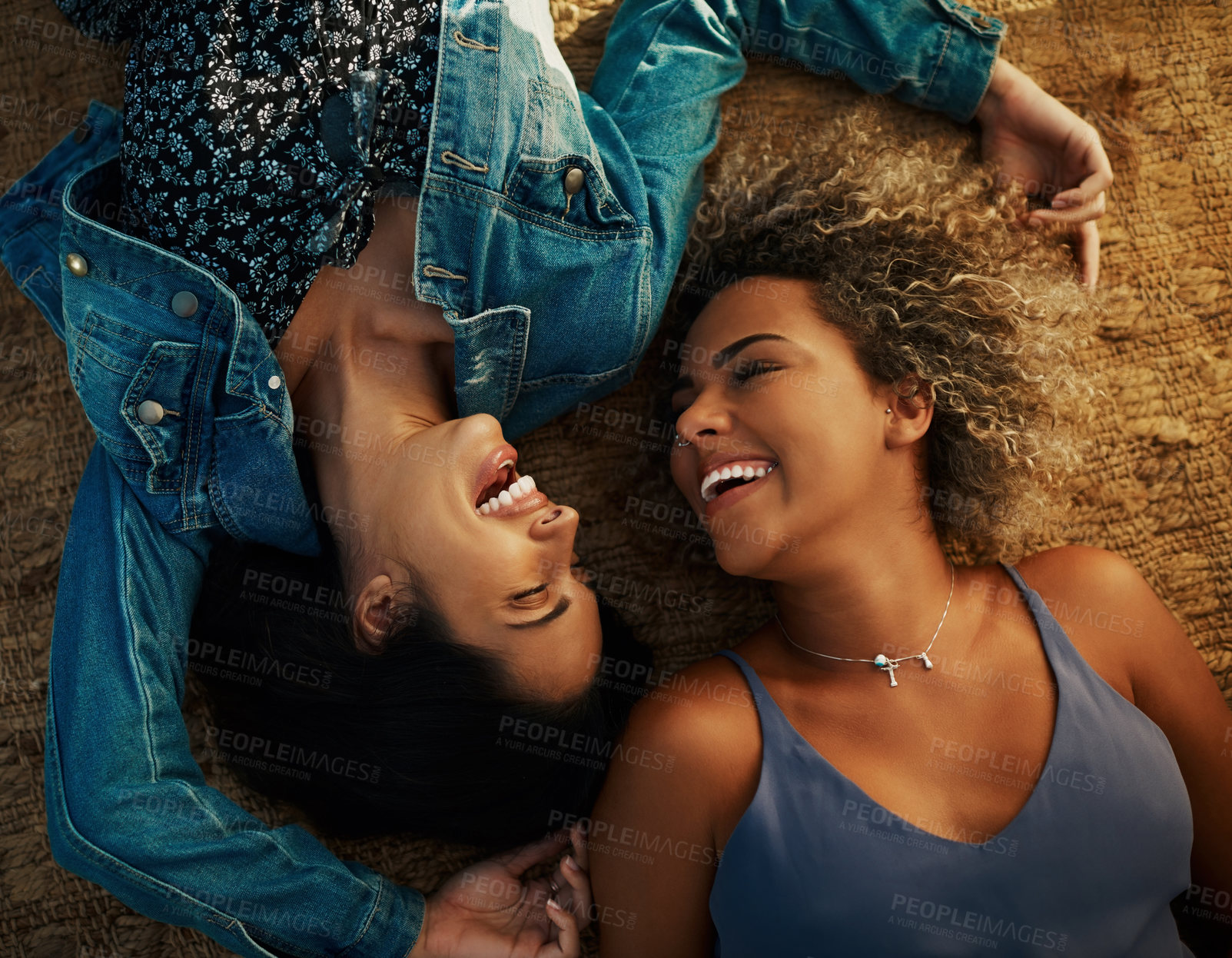 Buy stock photo High angle shot of two attractive young girlfriends smiling at each other while lying down at a park