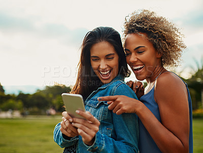 Buy stock photo Cropped shot of two attractive young girlfriends using a smartphone together while standing in a park