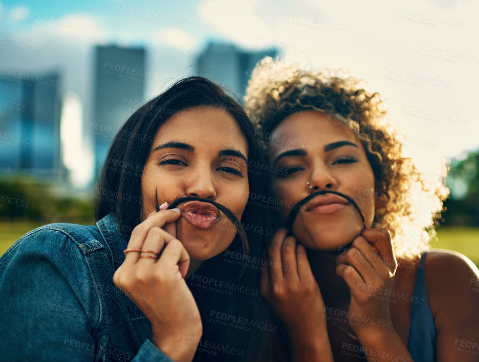 Buy stock photo Cropped portrait of two attractive young girlfriends making a moustache with their hair in a park