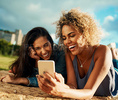 Buy stock photo Cropped shot of two attractive young girlfriends using a smartphone together while lying down at a park