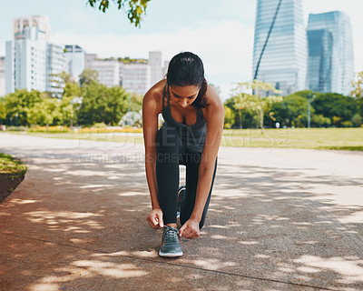 Buy stock photo Full length shot of an attractive young sportswoman tying her shoelaces outdoors in the city