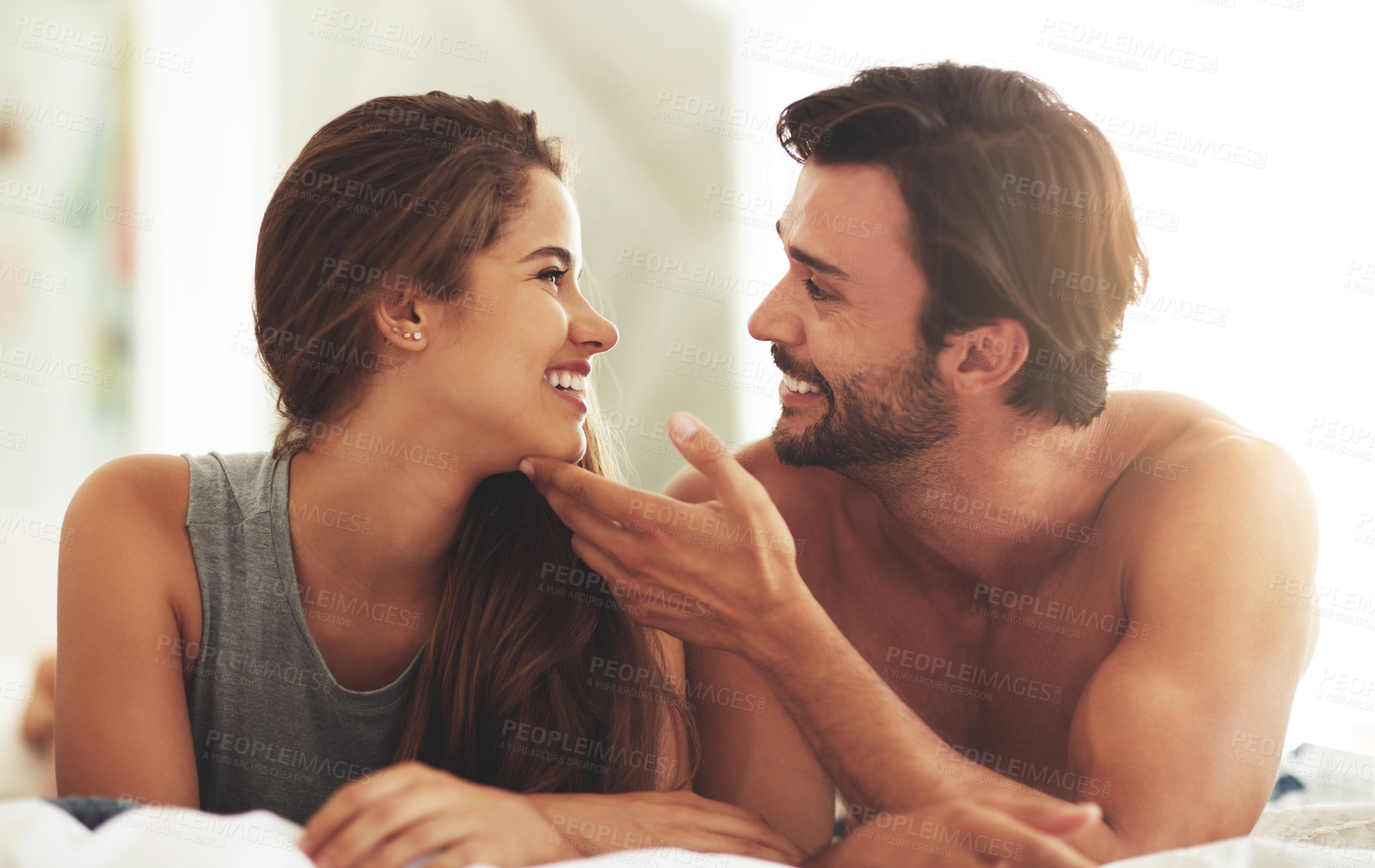 Buy stock photo Happy, couple and relax for love in bedroom with hand on chin for marriage commitment, romance and bonding. Smile, woman and man with support of trust, healthy relationship and care together at house