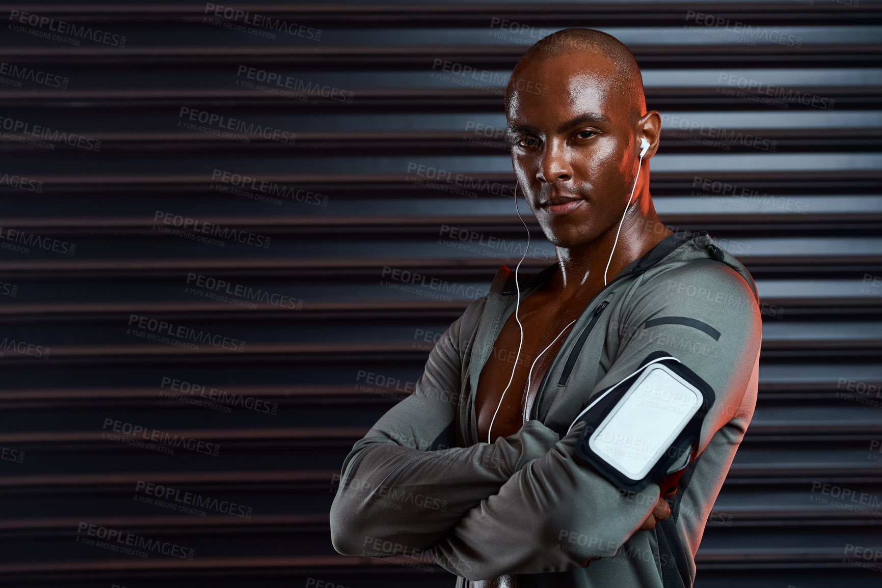 Buy stock photo Studio shot of an athletic young man posing with his arms folded while listening to music against a grey background