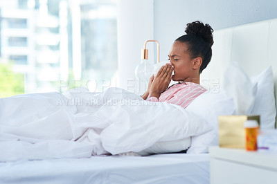 Buy stock photo Shot of a sickly young woman blowing her nose with a tissue in bed at home