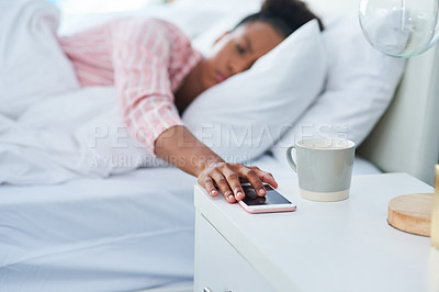 Buy stock photo Shot of an attractive young woman in bed reaching out for her phone on the dresser at home