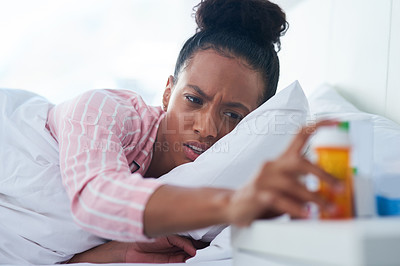 Buy stock photo Shot of an attractive young woman in bed reaching out for her medication on the dresser at home