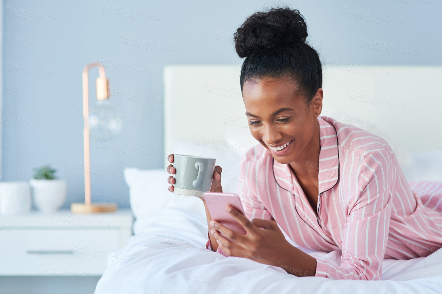 Buy stock photo Shot of an attractive young woman drinking coffee while using her cellphone in bed at home