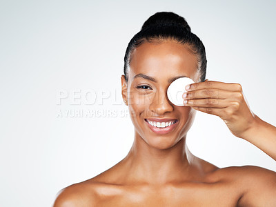Buy stock photo Studio portrait of an attractive young woman holding a cotton pad in front of her one eye while standing against a grey background