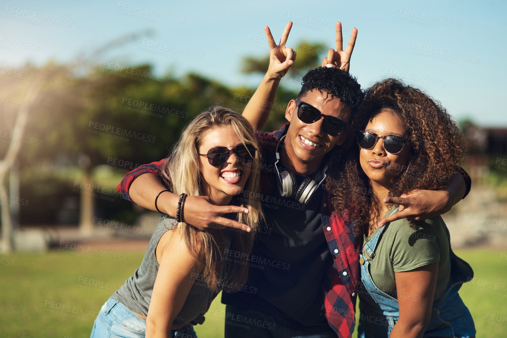 Buy stock photo Portrait of a group of cheerful young friends posing for a photo together while wearing sunglasses outside in a park